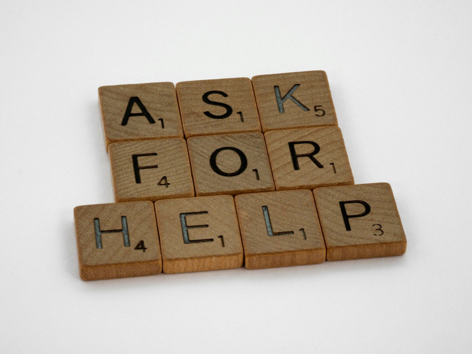 Wooden Scrabble tiles on a white surface spelling 'Ask for Help' in a conceptual layout.